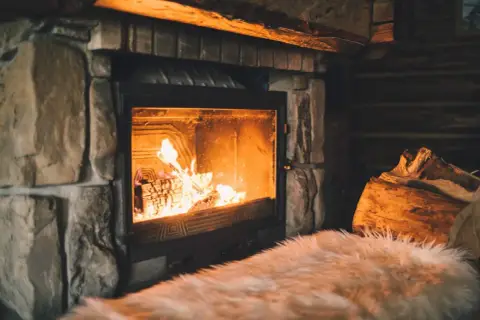 Un feu crépite joyeusement dans une cheminée en pierre, réchauffant l'atmosphère d'un chalet rustique. Des bûches attendent patiemment à côté.