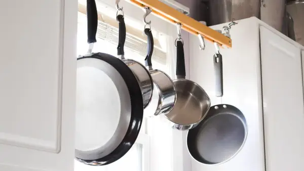 Une astuce rangement casserolier : des poêles suspendues à une barre en bois, libérant de l'espace dans les placards.